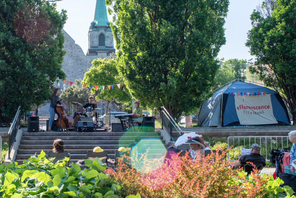 Photo d'une scène, l'été, avec musicien-nes et affiche "effervescence citoyenne"